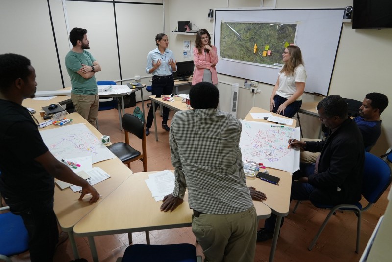 A mixed group of Hub researchers discussing social mapping whilst stood around diagrams and illustrations